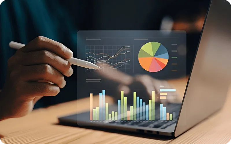 Hand pointing with stylus at digital charts including line, pie, and bar graphs over laptop keyboard.