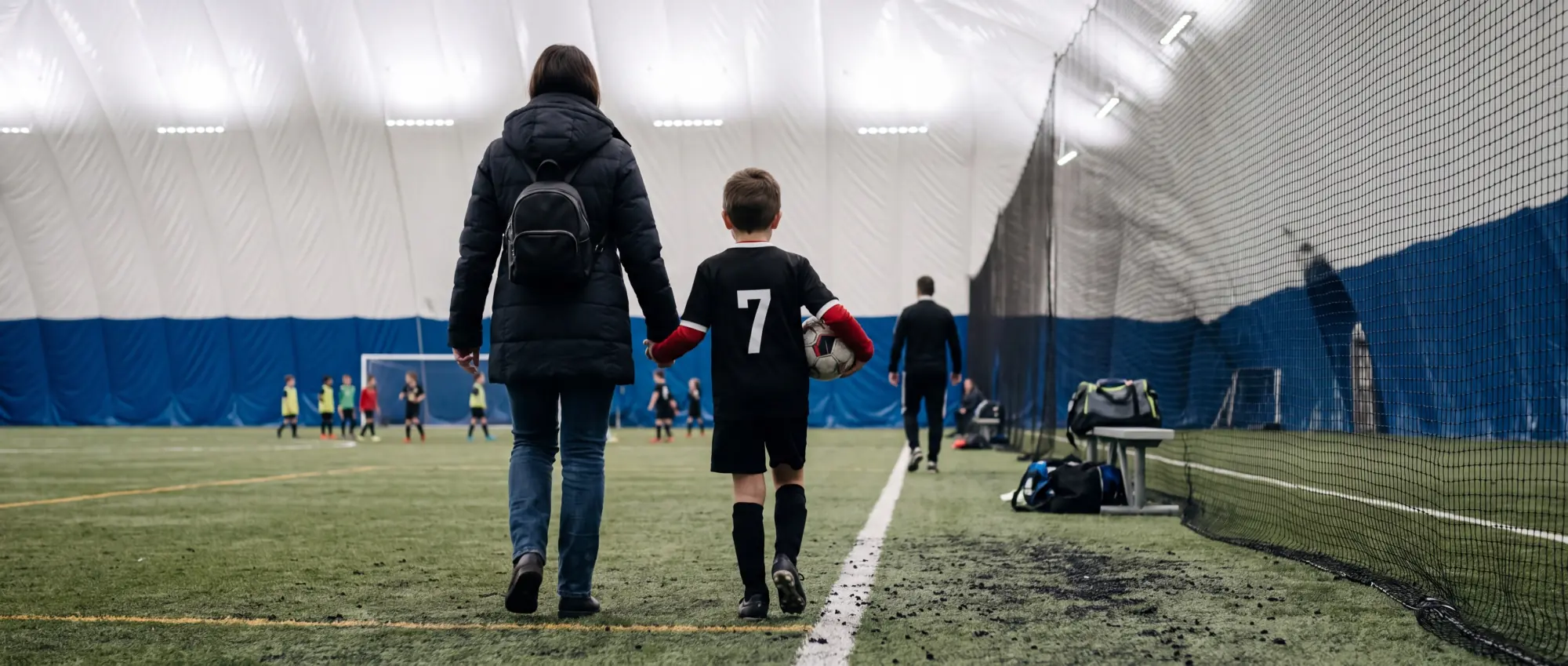 Un parent et son enfant en chandail de l’AS Laval marchent main dans la main vers le terrain, vus de dos