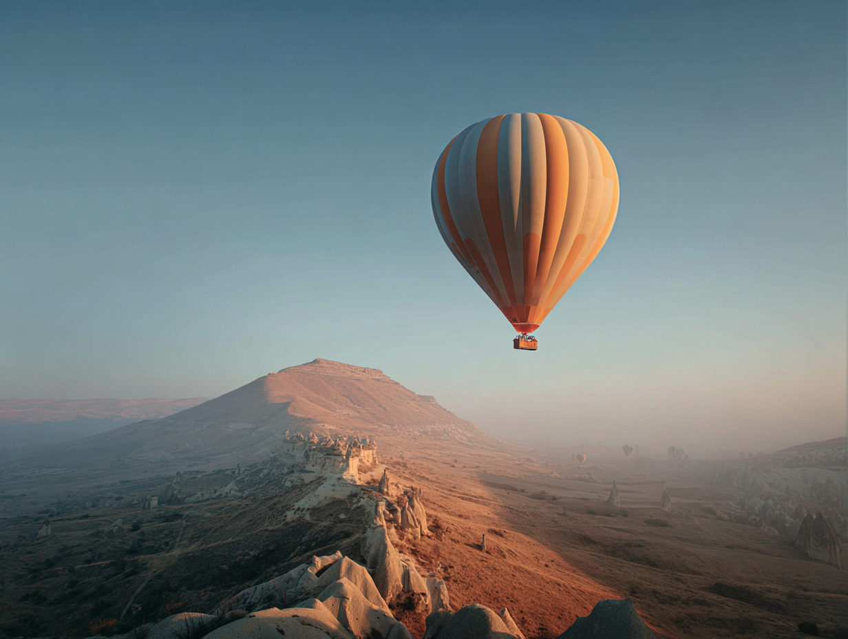 Orange and white striped hot air balloon floating over a rocky landscape with a mountain in the background at sunrise.