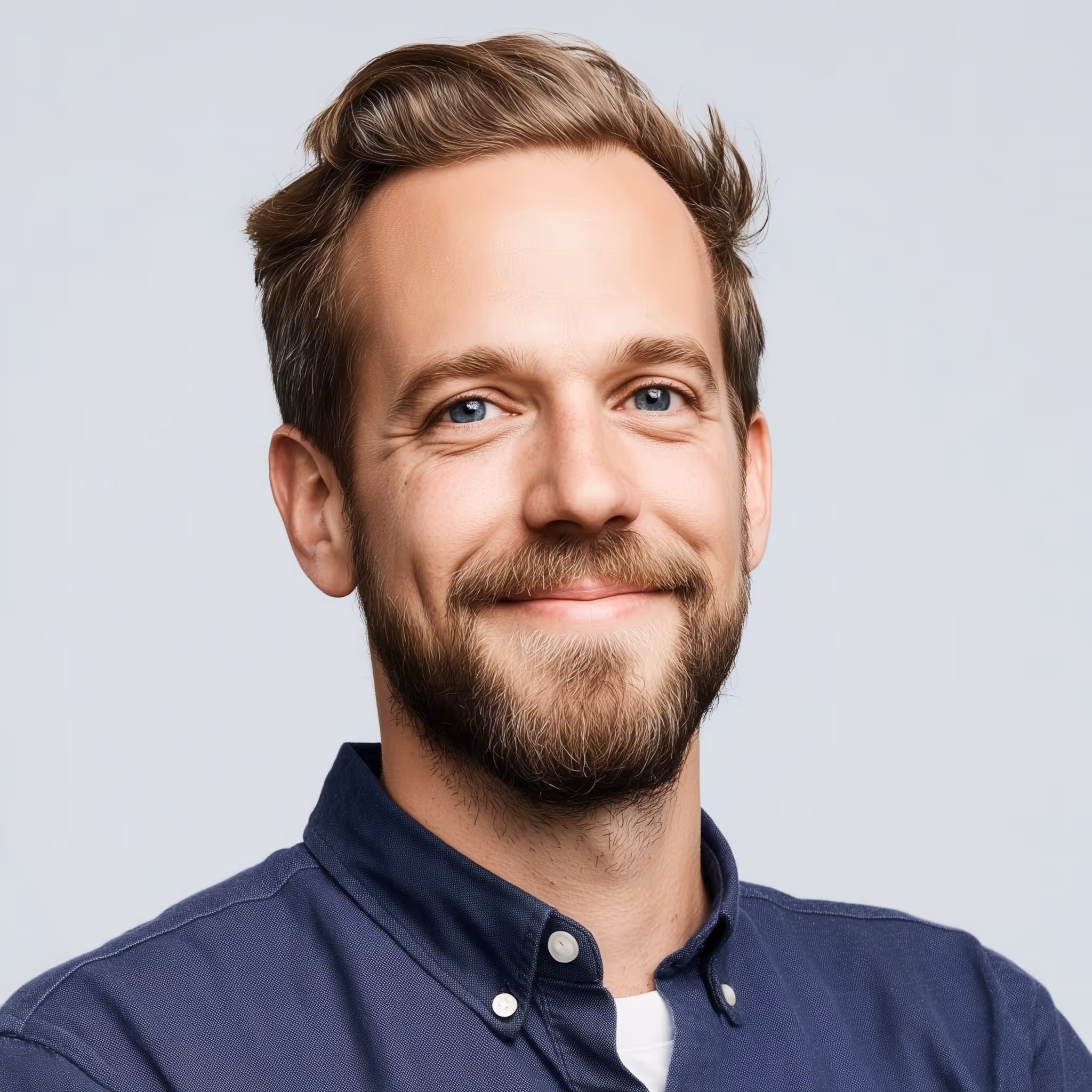 Smiling young man with light brown hair, beard, and blue eyes wearing a navy button-up shirt.