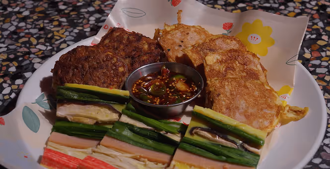 Plate with assorted jeons (Korean pancakes) and a small metal bowl of dipping sauce.
