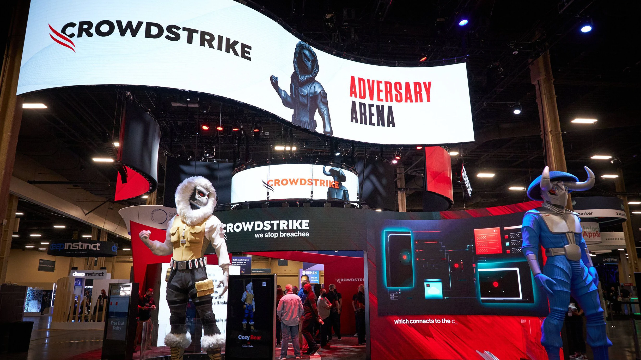OOH conference design at Black Hat or RSA conference. CrowdStrike exhibit with large digital screens and two armored character statues at a technology conference.