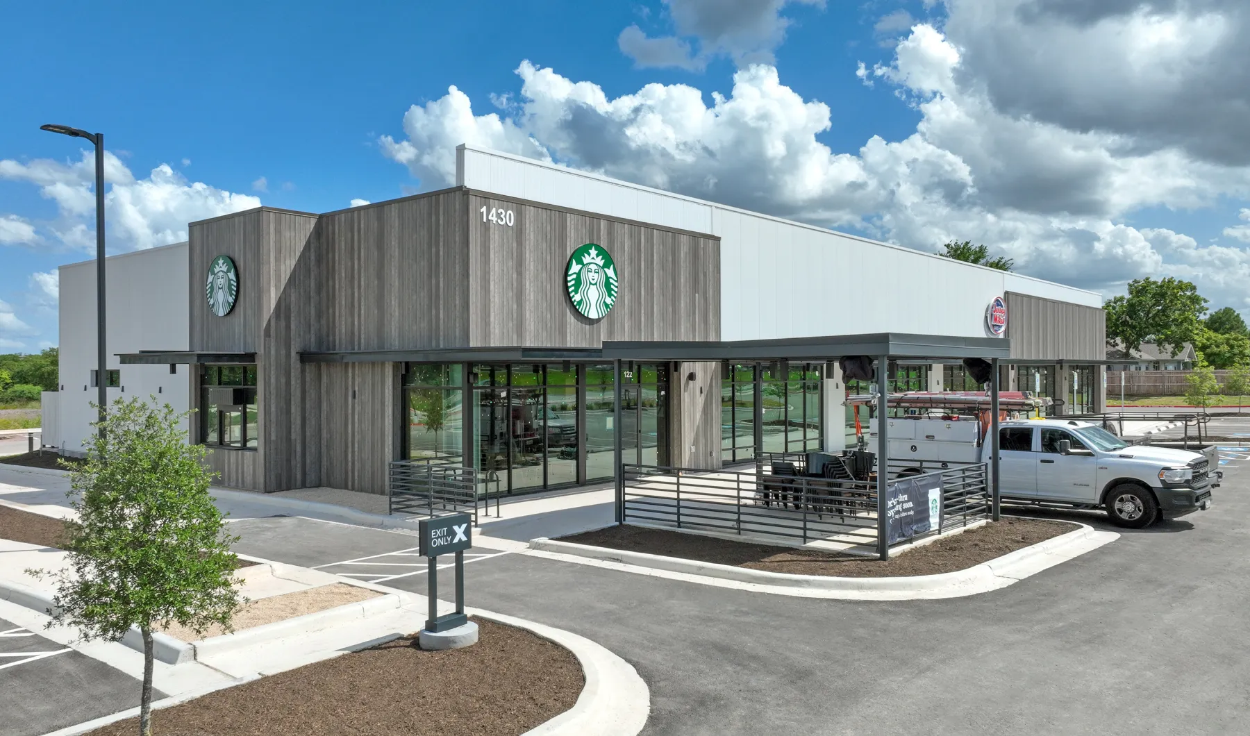 Modern Starbucks building with wood paneling and large windows under a blue sky with clouds, beside an adjacent Burger King.