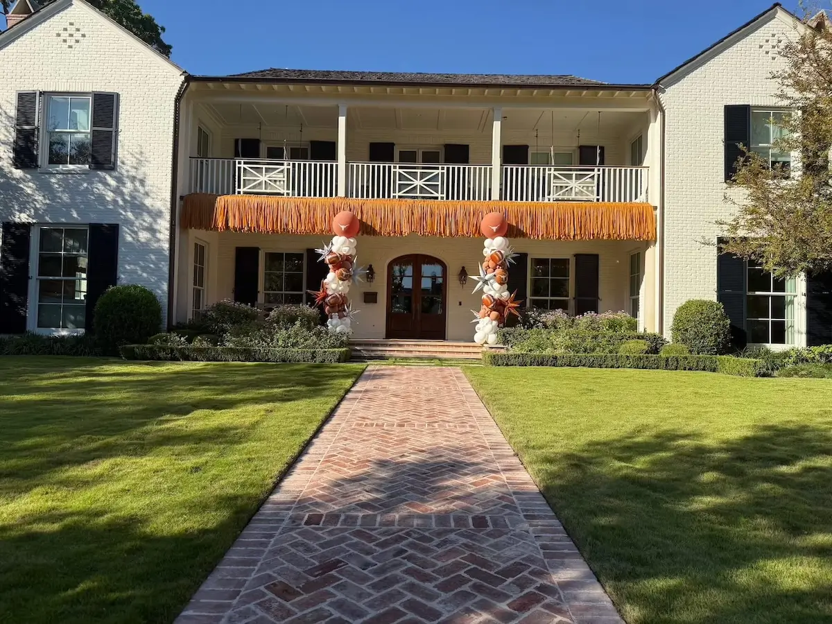 Burnt orange fringe streamer garland on Highland Park home in Dallas hanging from the balcony