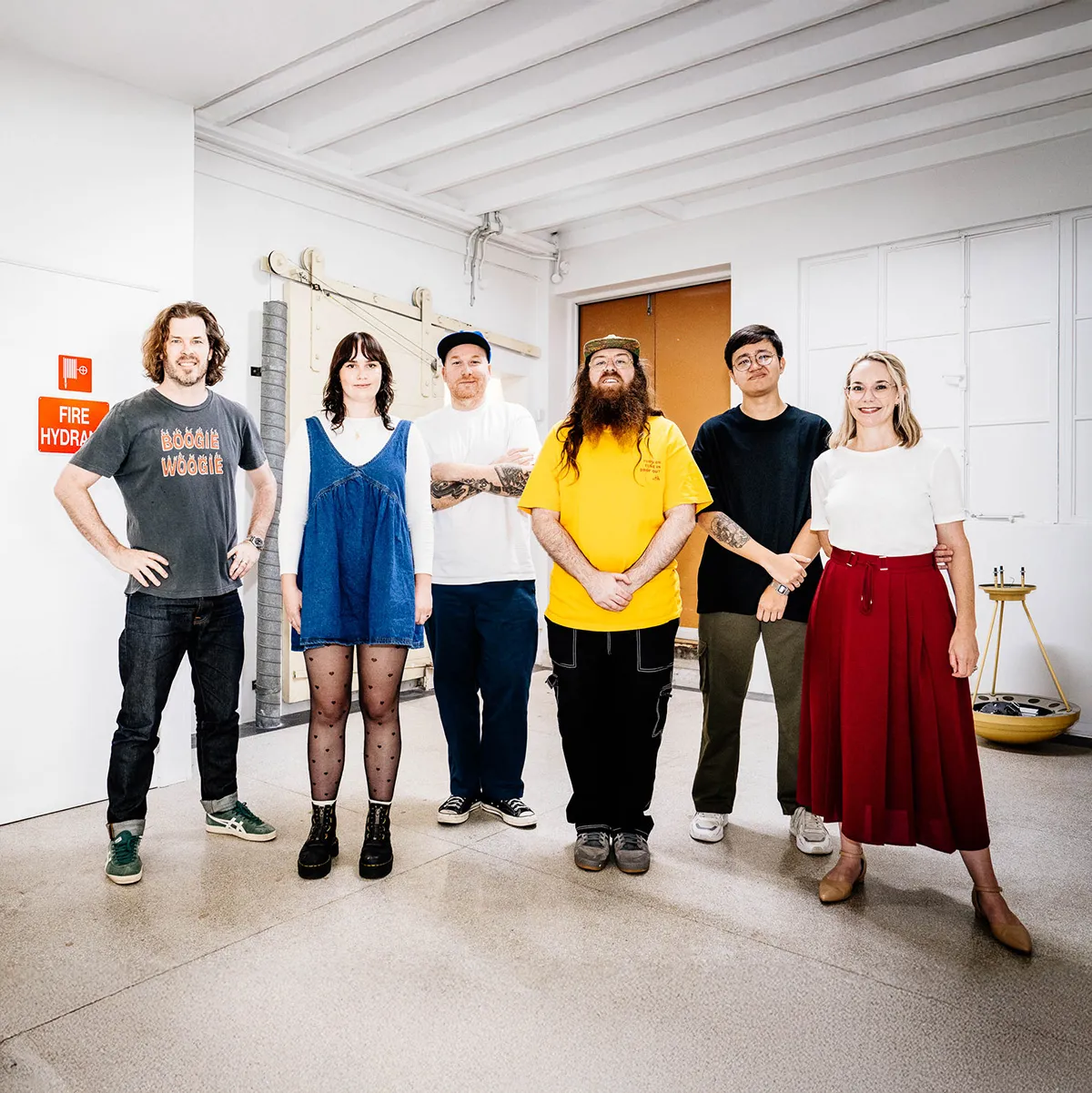 Six people standing indoors against a white wall, smiling and facing the camera.