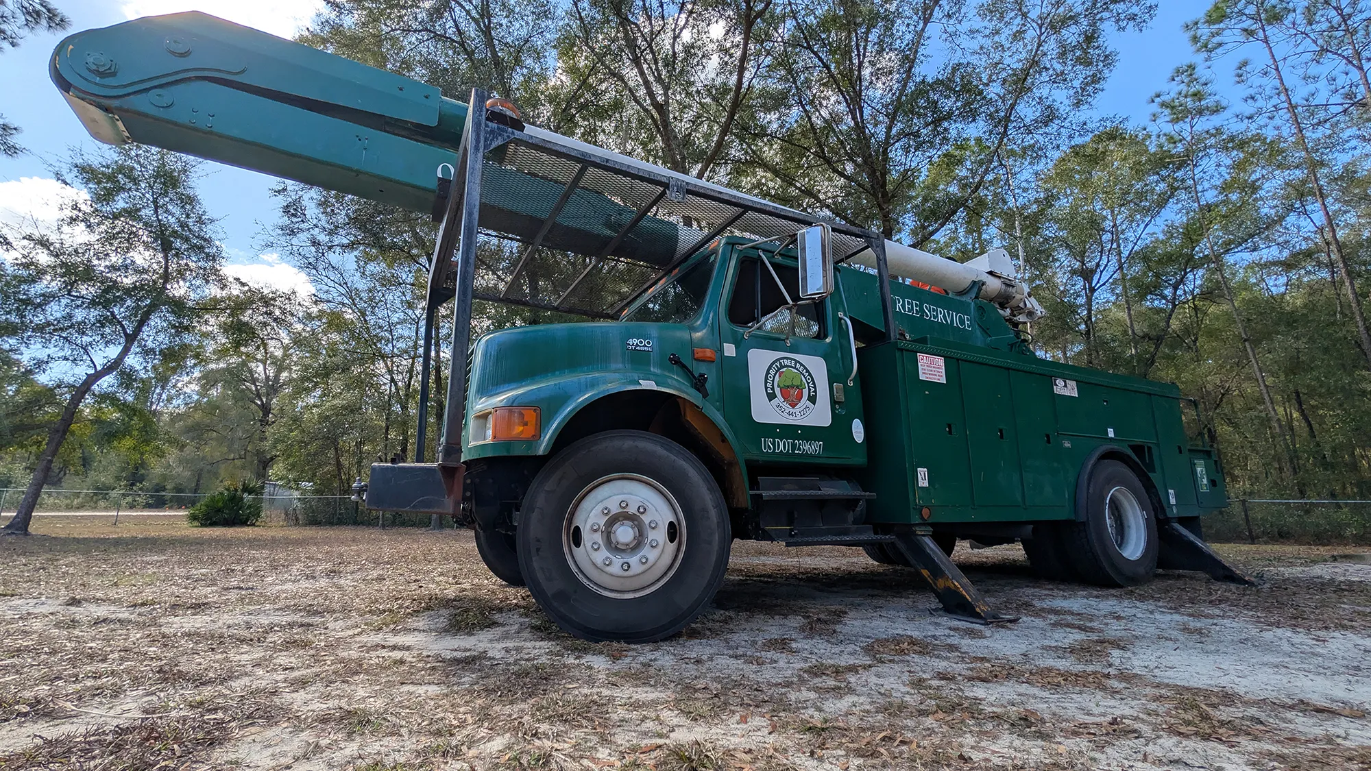 Priority Tree Removal green bucket truck parked under mature Florida trees