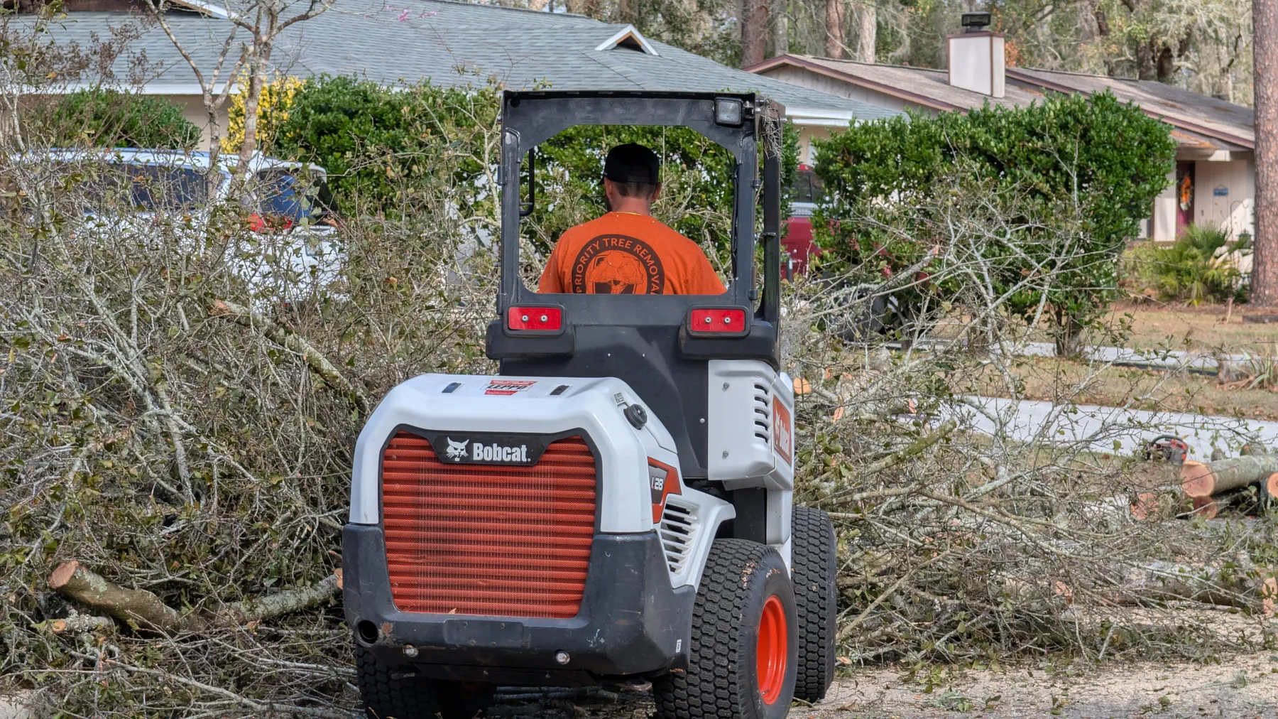 Priority Tree Removal mini loader moving tree debris while protecting a residential property.