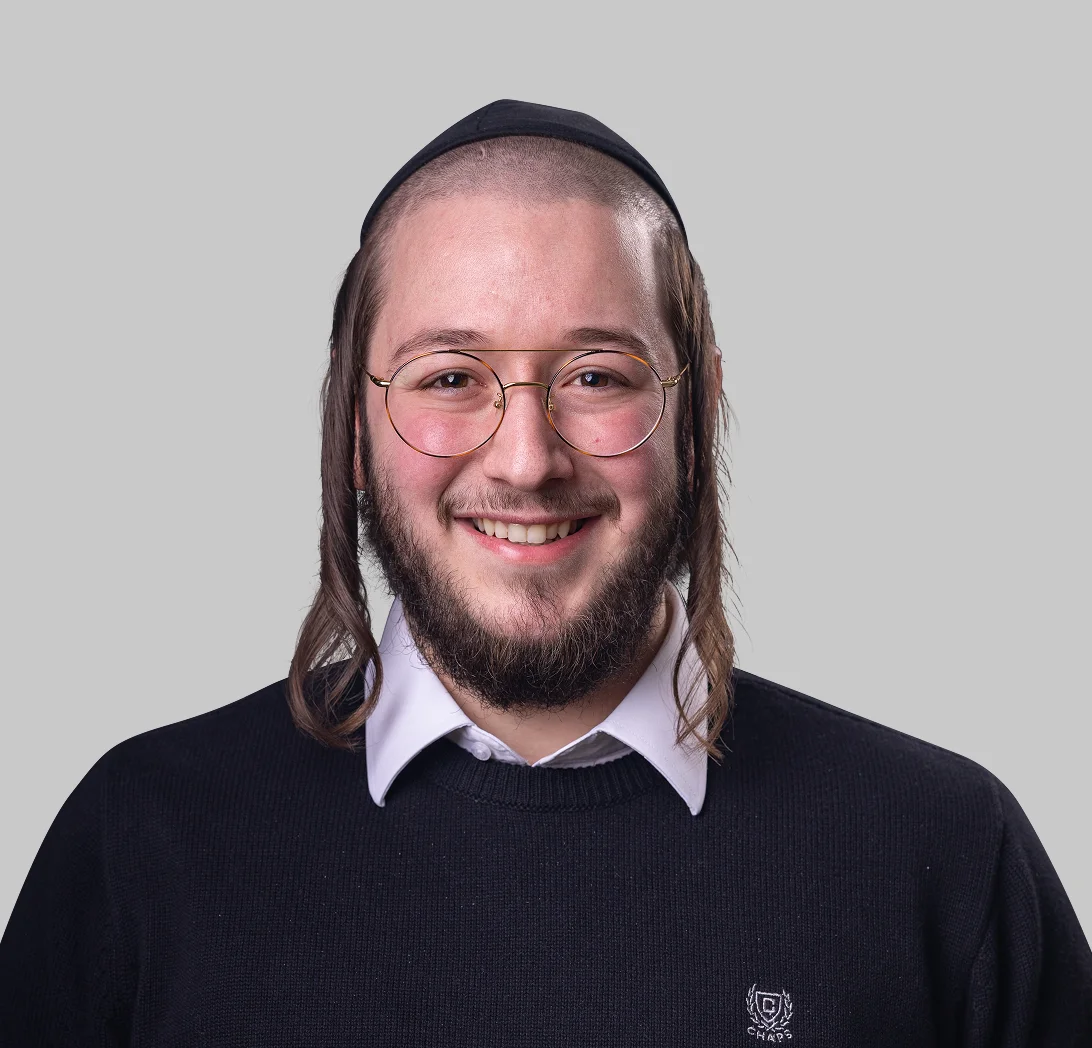 Smiling man wearing round glasses, a kippah, and a dark sweater over a white collared shirt, with curly sidelocks.