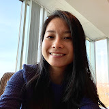 Thu Vu - smiling young woman with long dark hair sitting indoors near large windows with natural light.