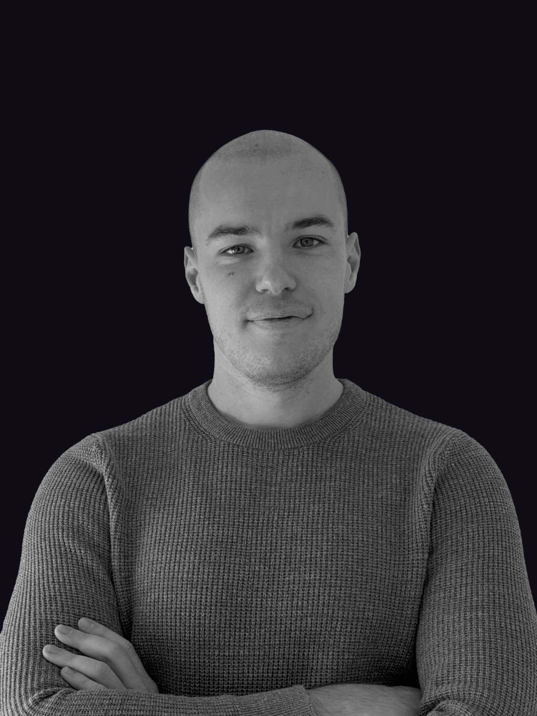 Marko Zivic CEO - Portrait of a smiling bald man with arms crossed wearing a textured sweater against a dark background.