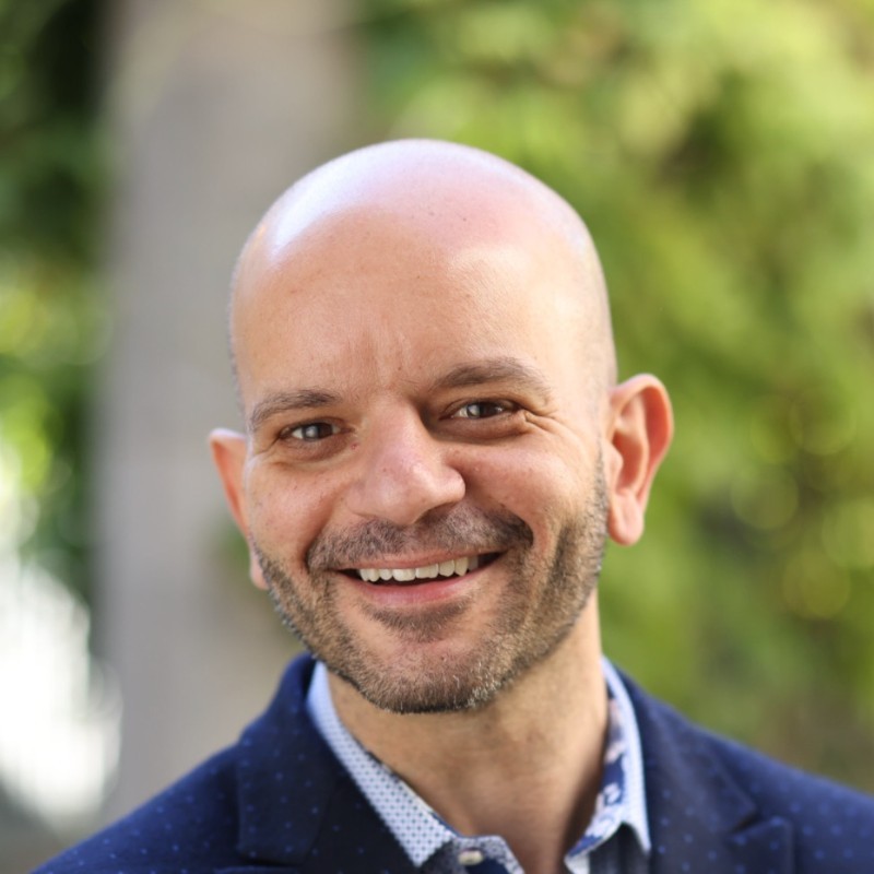 Smiling professional woman in a brown suit holding a resume and a red folder in an office setting.