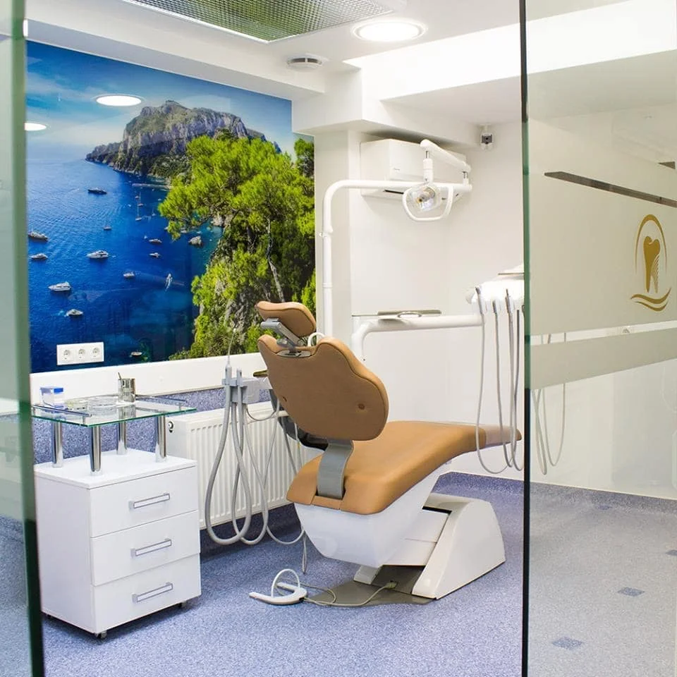Modern dental clinic room with a tan dental chair, white equipment, and a mural of a coastal landscape with blue sea and boats on the wall.