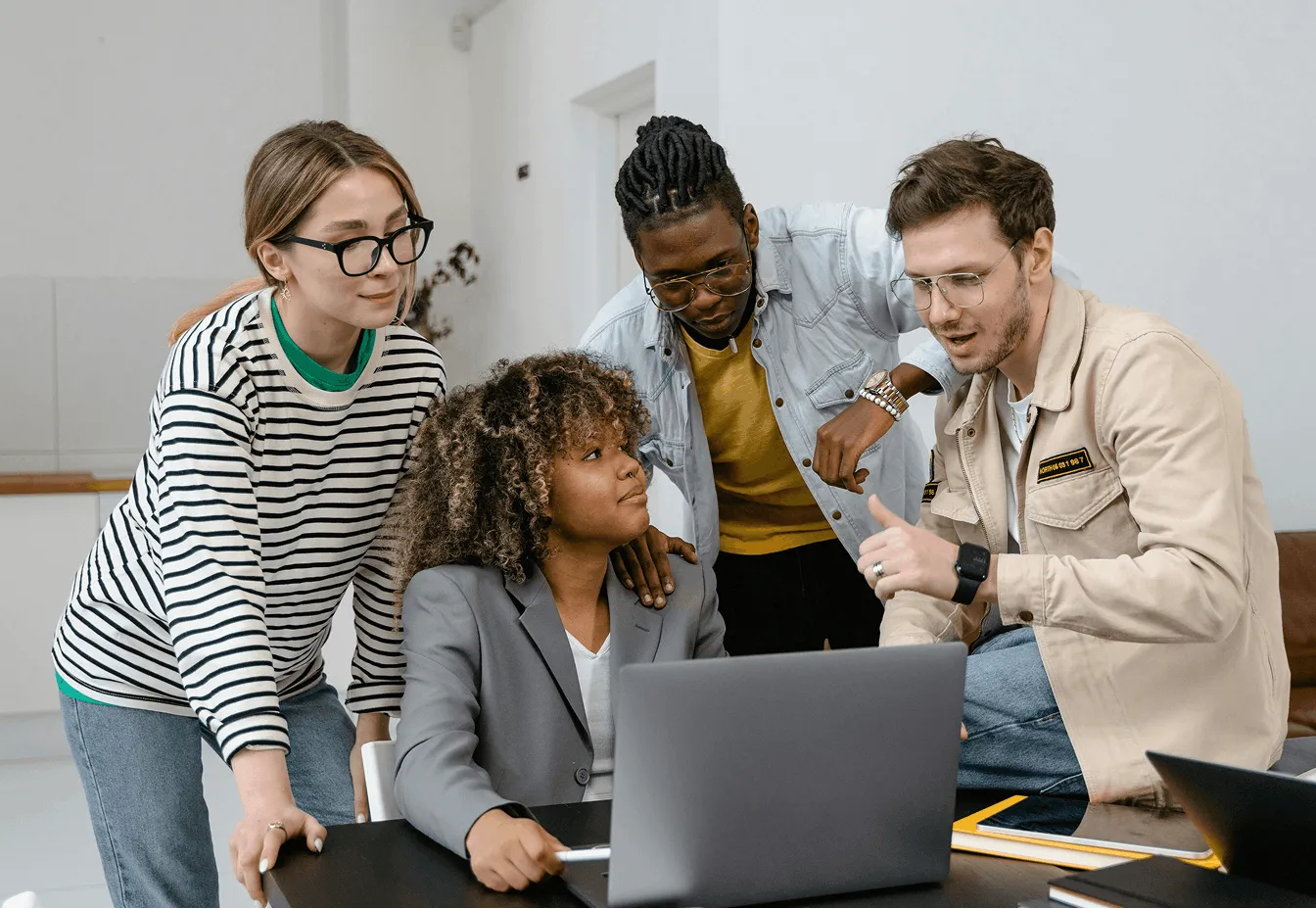Group of four diverse young professionals collaborating around a laptop in a modern office.
