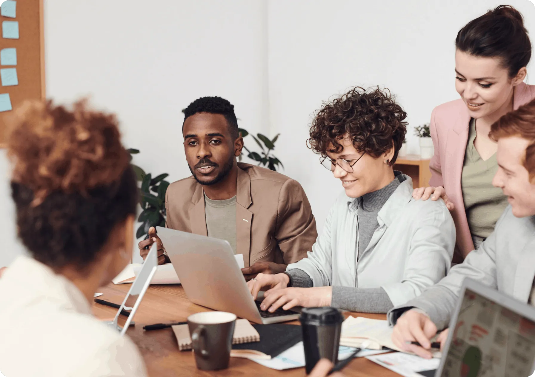 Four diverse colleagues collaborating and discussing work around a table with laptops and coffee cups.