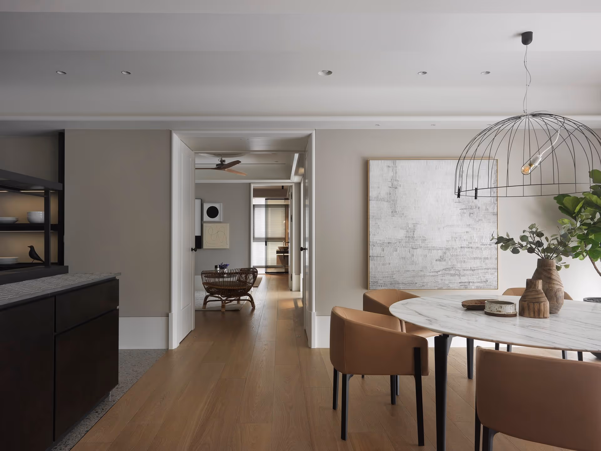 Modern dining area with round marble table, brown chairs, abstract wall art, and large wire pendant light.