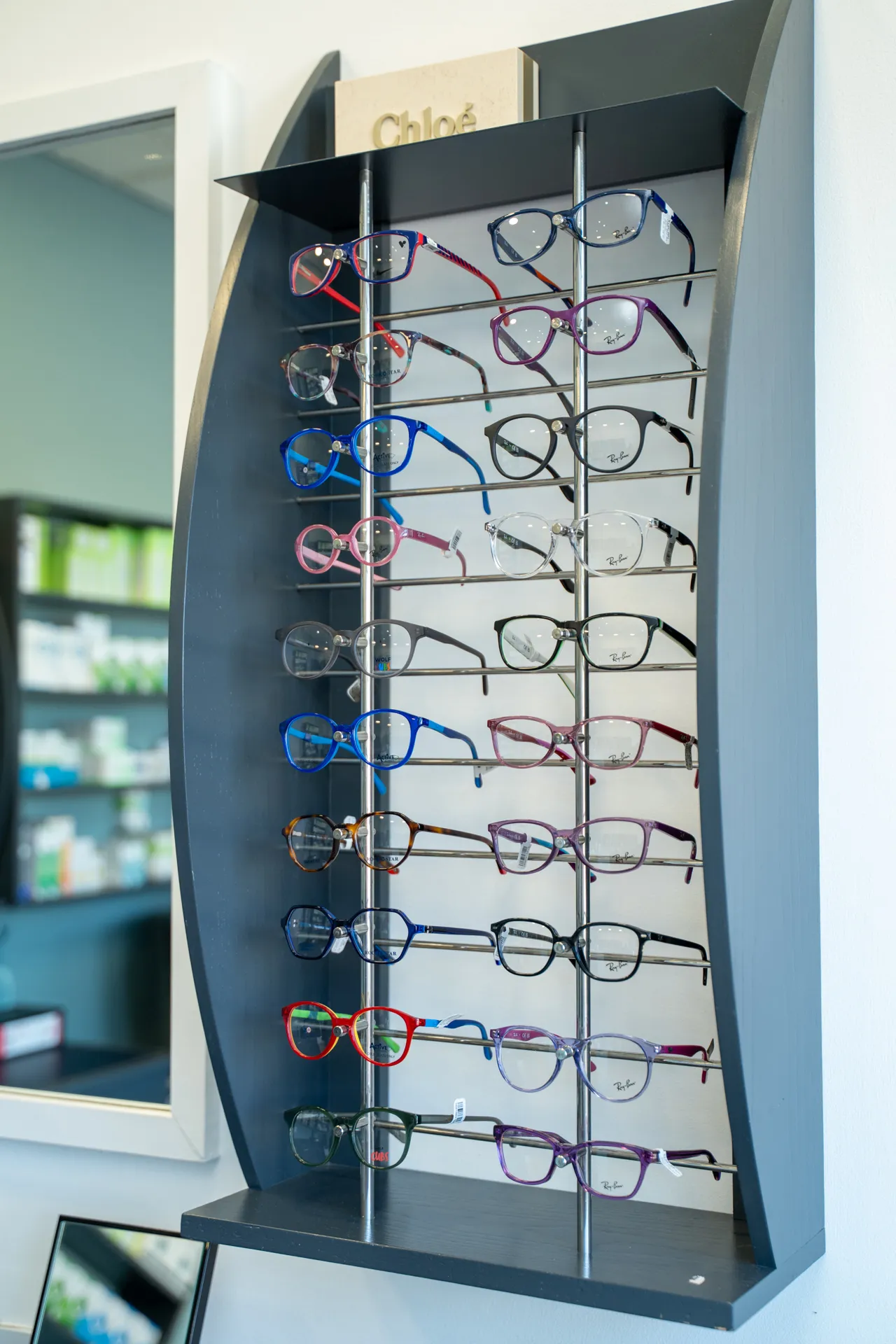 Display rack with multiple pairs of colorful eyeglasses in an optical store, with a Chloé sign on top.