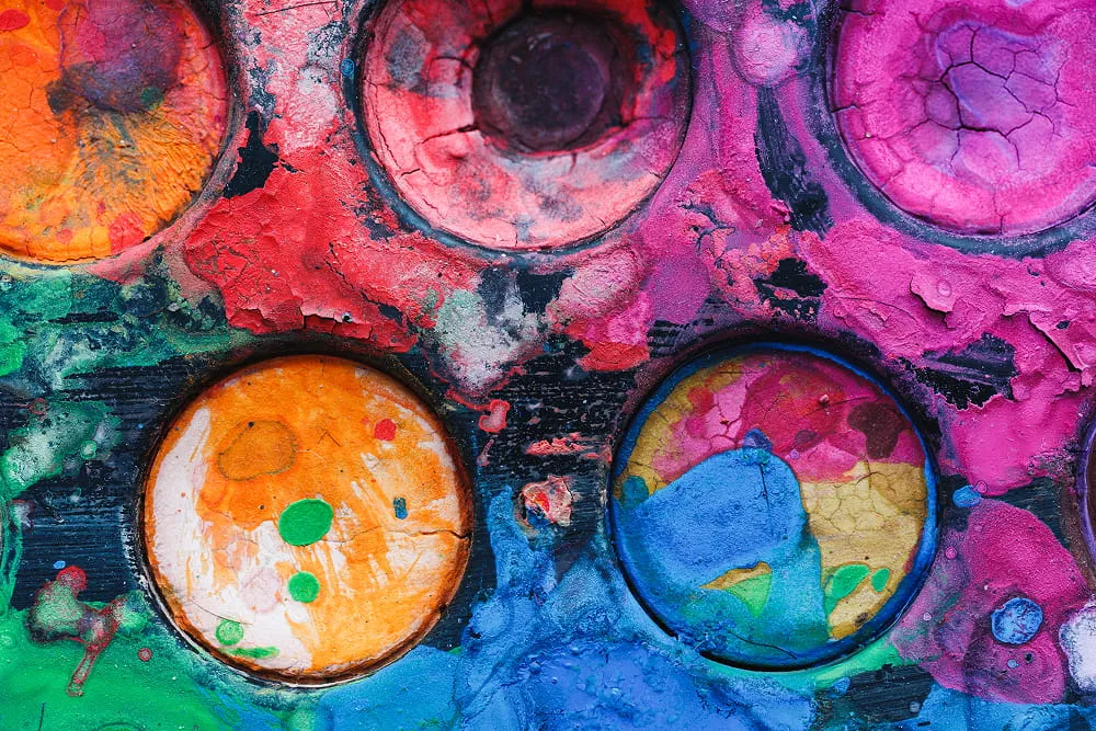 Close-up of a cracked and textured watercolor paint palette with vibrant colors including orange, pink, blue, and green.