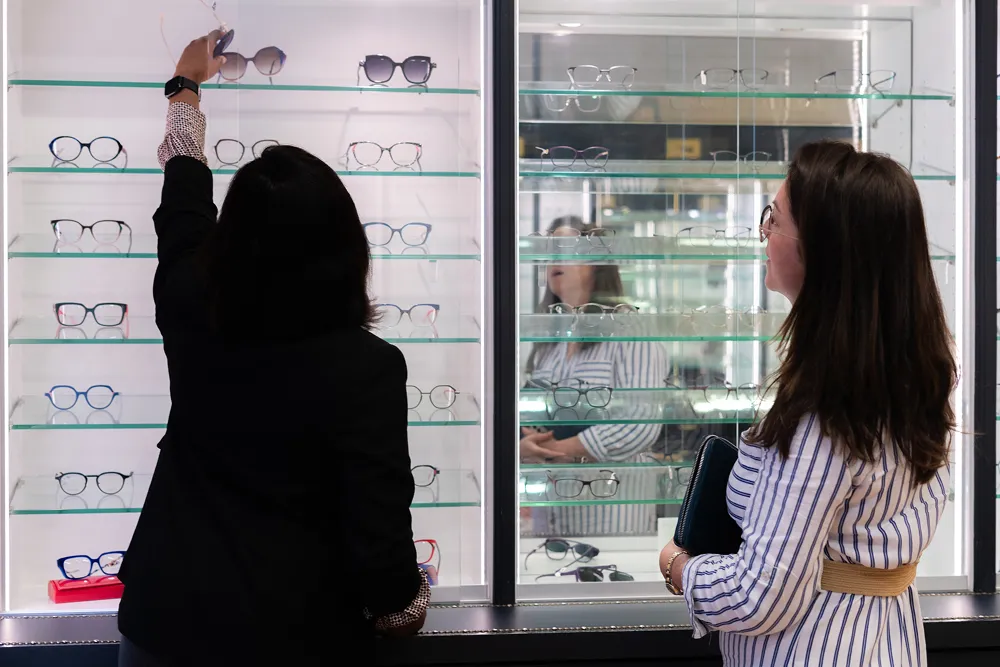 Two women selecting eyeglasses from a glass display at an optical store.