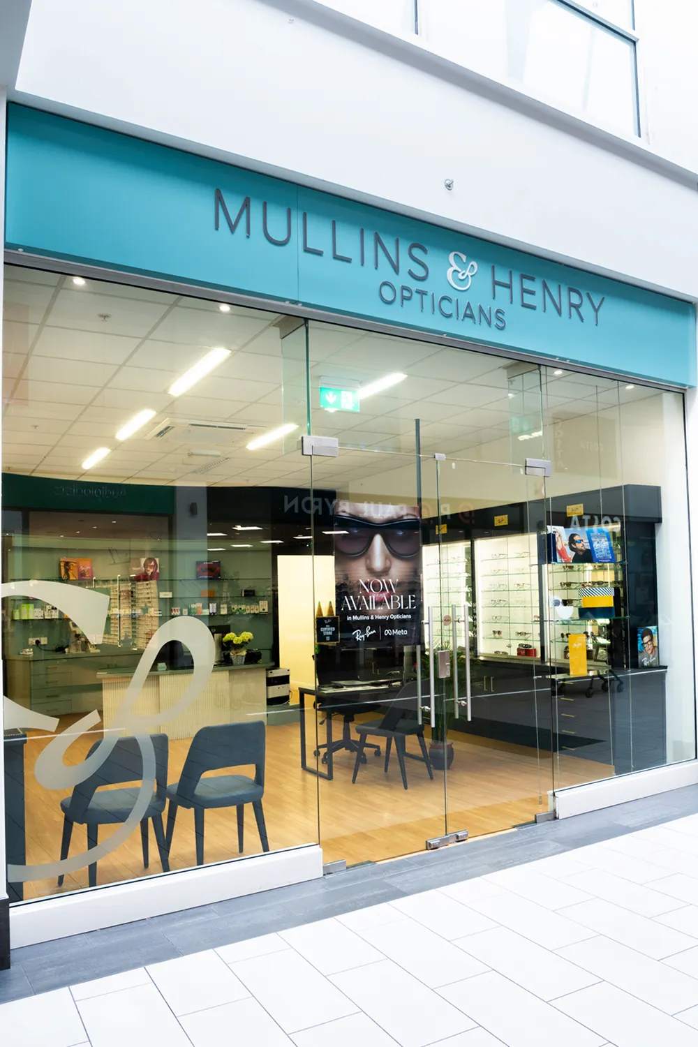 Exterior view of Mullins & Henry Opticians store with glass doors and interior chairs and eyewear displays.