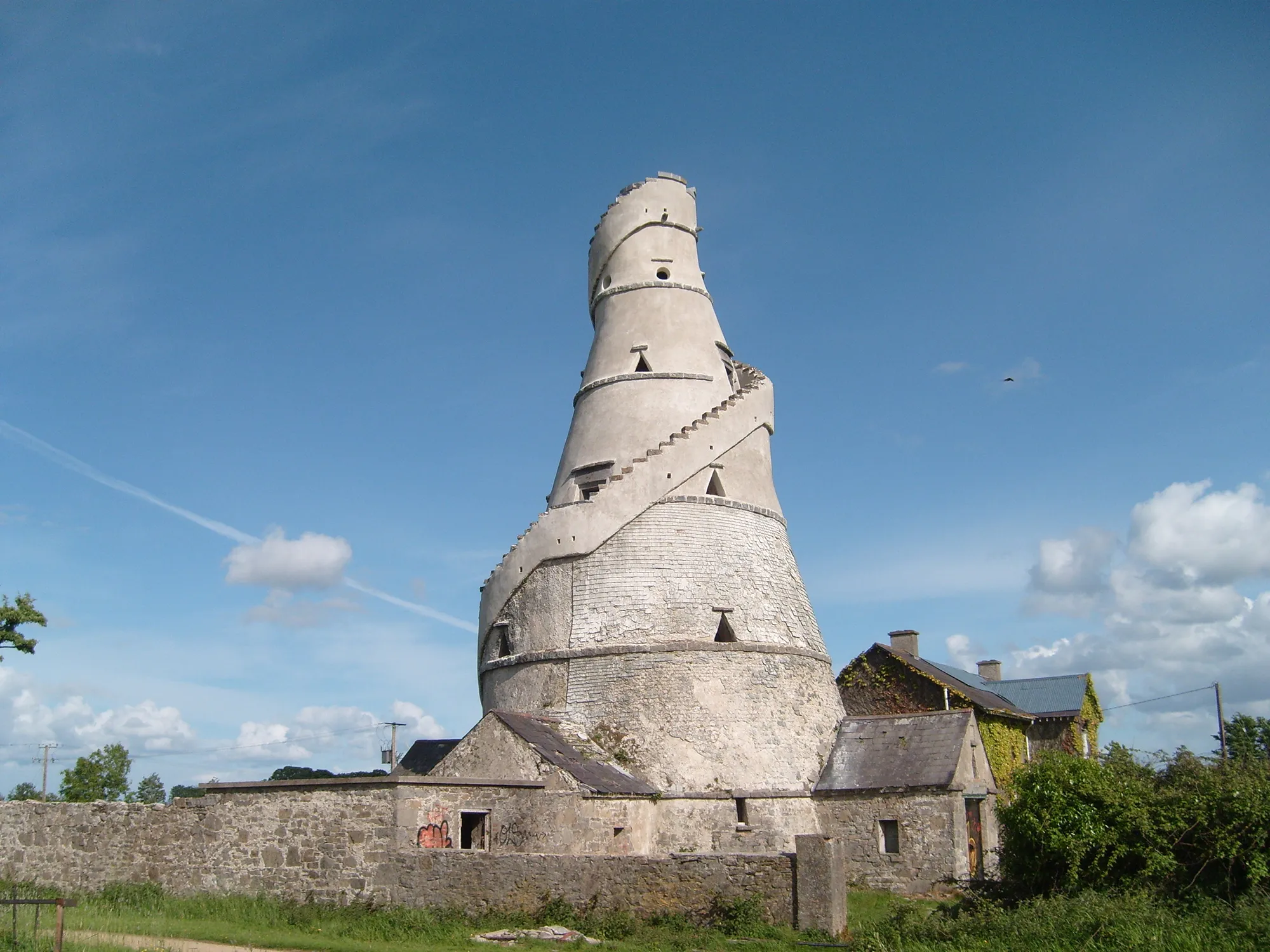 Ancient stone tower with a spiral staircase wrapping around it under a blue sky.