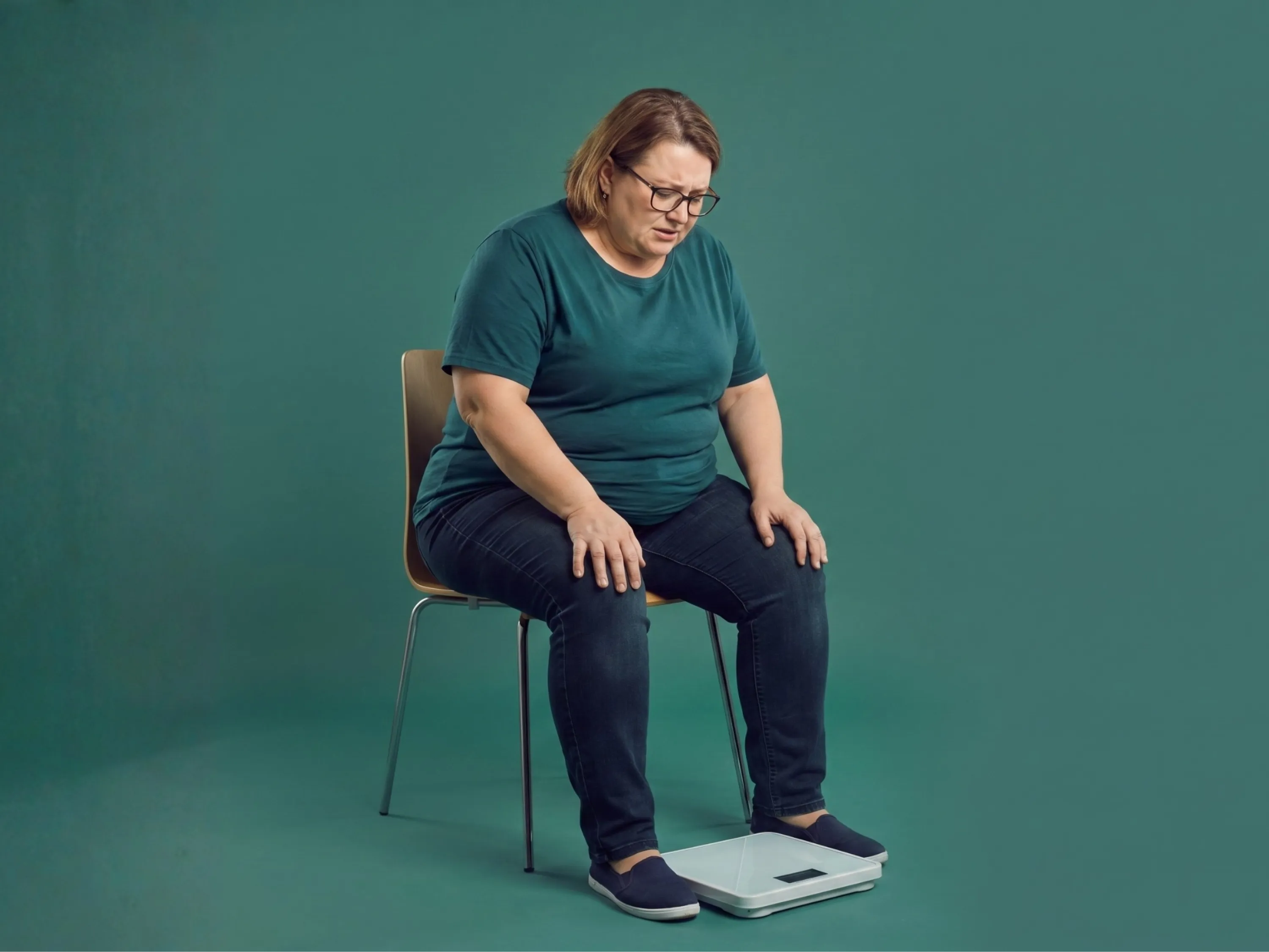 Femme en surpoids assise devant une balance, illustrant la prise de poids pendant la ménopause.