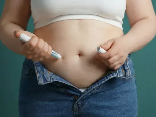 Une femme s'injecte du Wegovy dans le ventre à l'aide d'un stylo, sur fond vert.