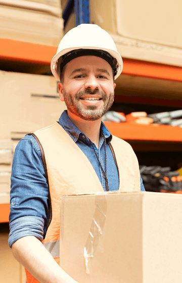 Пакувальник у білій касці та світло-оранжевій жилетці посміхається, тримаючи коробку в руках.