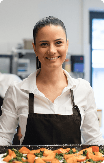 Офіціантка в чорному фартусі та білій сорочці тримає тацю з блюдом.