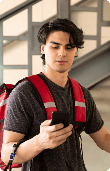 Молодий хлопець-кур'єр з рюкзаком для доставки дивиться на екран смартфону