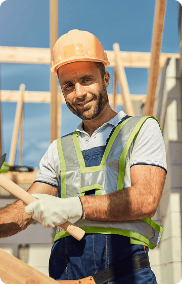 Чоловік-будівельник у жовтому захисному шоломі, світлій футболці та жилеті із світловідбивачами на будівельному майданчику, тримає дерев'яний інструмент.