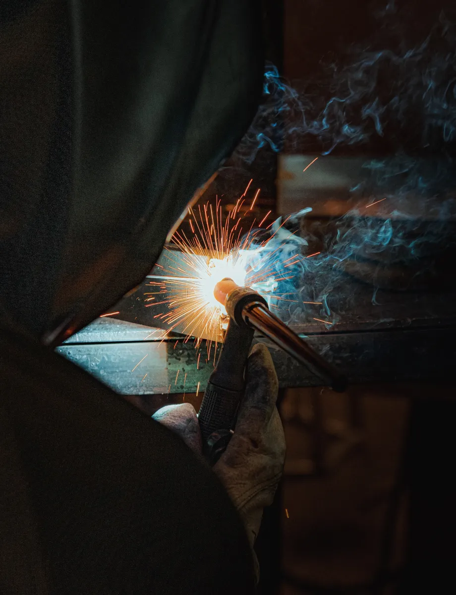 Person welding metal with sparks and smoke visible around the welding torch.