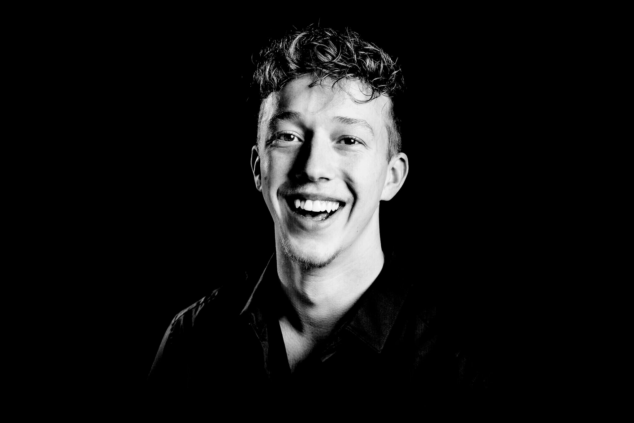 Zwart-wit portret van een glimlachende man in een donker shirt.