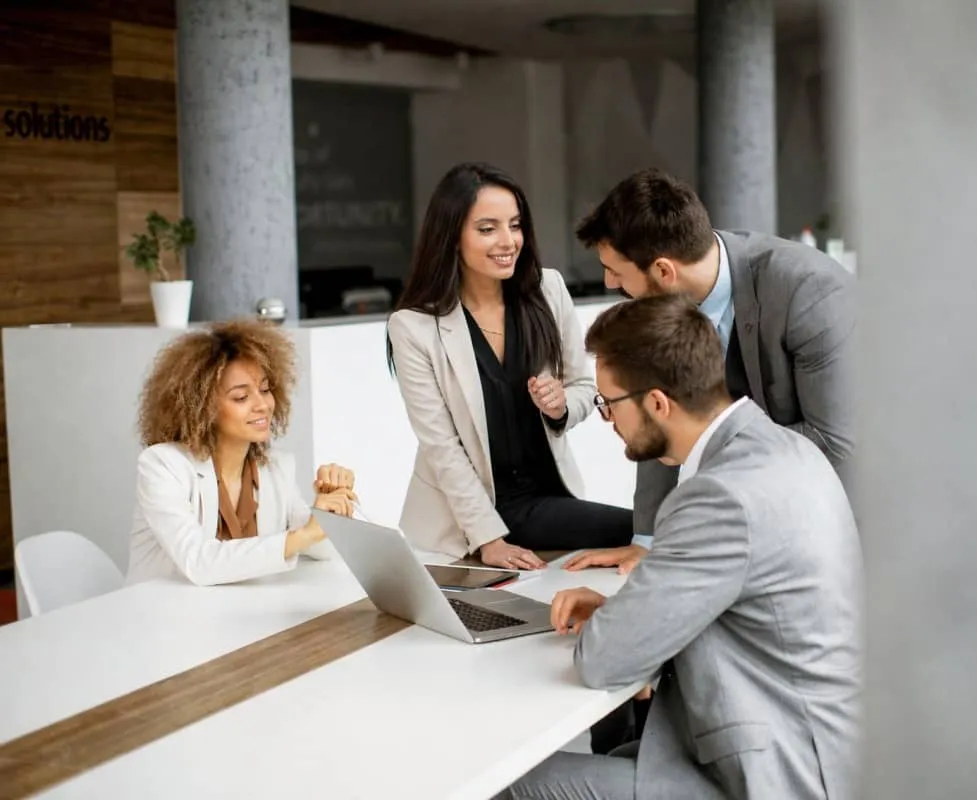 Quatre professionnels en réunion autour d'un ordinateur portable dans un bureau moderne de chez leadvalue.