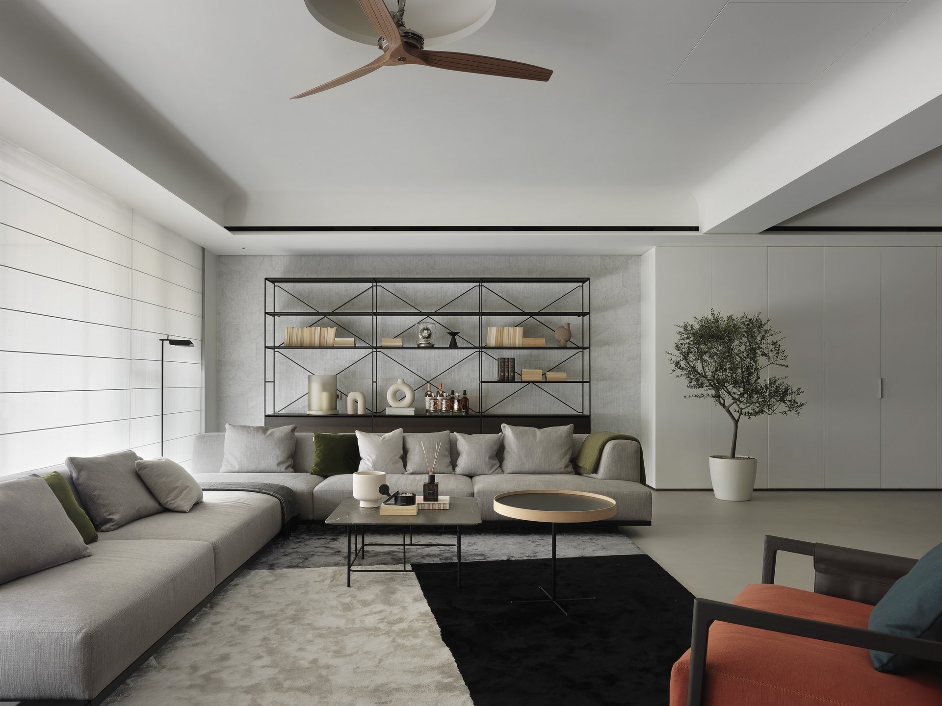 珥本設計｜BOFFI HOME II 客廳完整景：黑鐵X字幾何書架陳列典籍與器皿，灰色L型沙發與橙色布藝扶手椅圍出會客核心，金色圓茶几與雙色地毯拉出材質層次