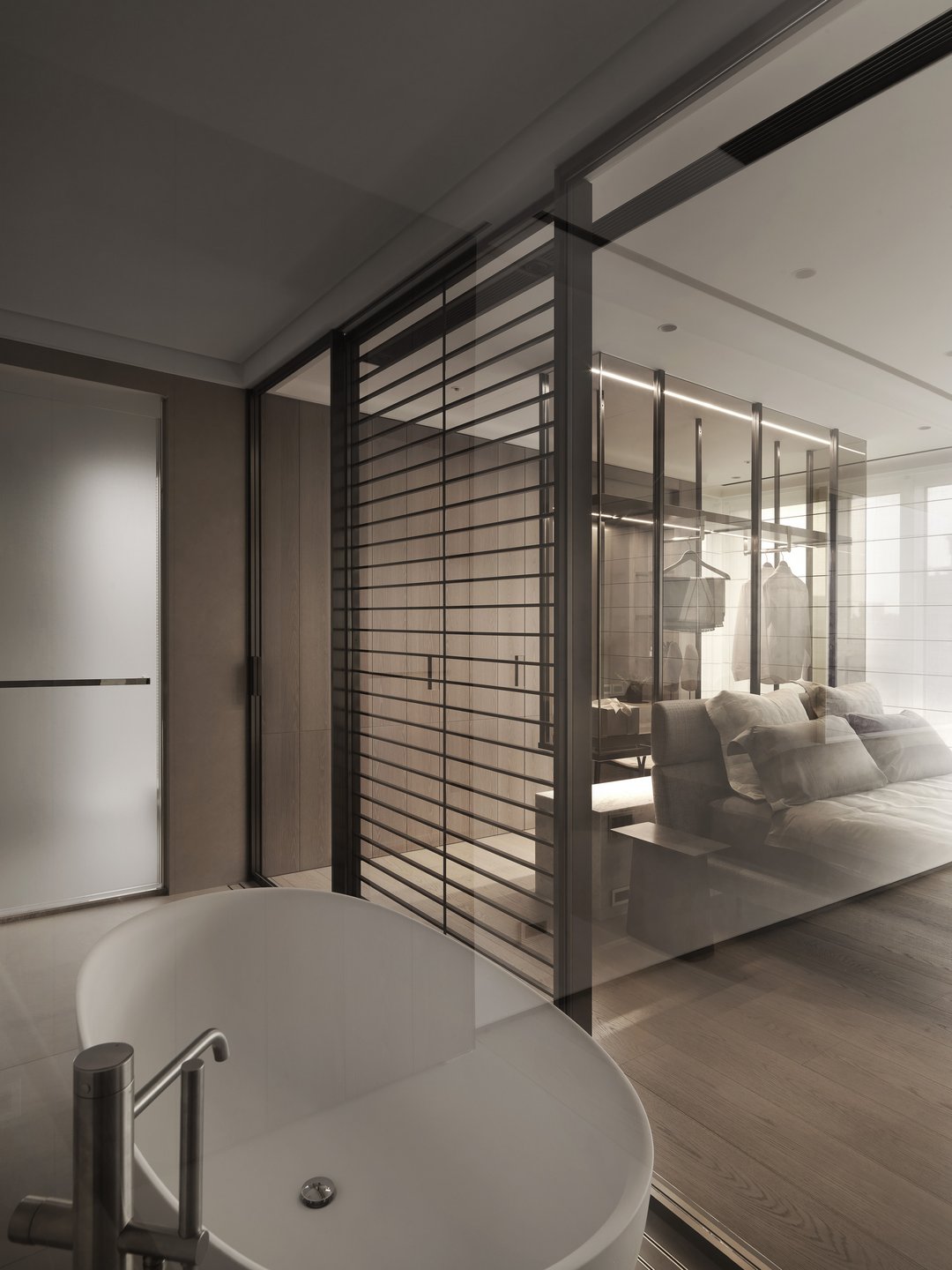 珥本設計｜BOFFI HOME II 主浴至主臥穿透景：白色圓筒獨立浴缸居中，黑鐵橫線屏風與透明玻璃隔門一次穿透至主臥床與更衣間吊掛襱衫，動線於通透中界定領域