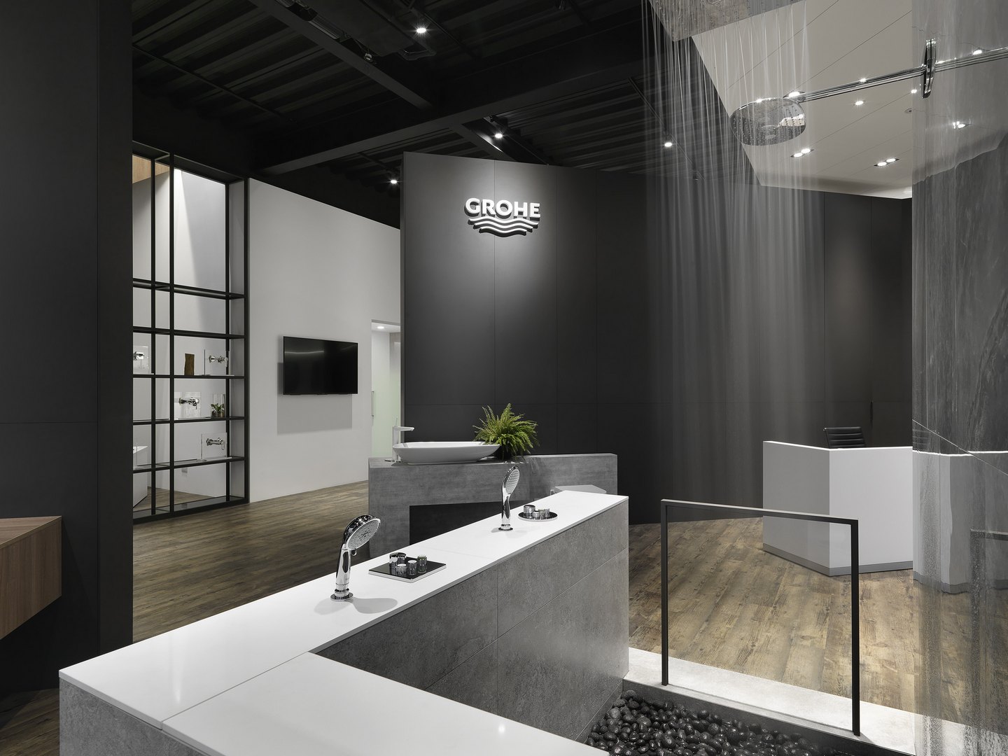 珥本設計｜鼎邑衛浴 GROHE 品牌展區：黑色高牆懸白色 GROHE 品牌 logo，前景灰色石材矮台陳列鍍鉻花灑手把，黑色磁磚水池填滿黑色鵝卵石，右側頂端花灑降下水柱示範，左側黑鋼格架櫃陳列龍頭