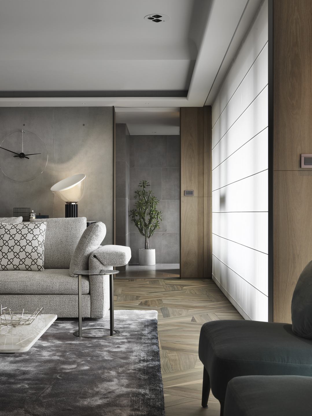 珥本設計|丽格 III 住宅客廳側景:MINOTTI 灰色沙發搭菱格紋抱枕與絨面單椅,Nomon 極簡大圓掛鐘與 Flos Taccia 桌燈於灰色清水模牆錨定,深綠絲絨扶手椅坐落於窗邊。