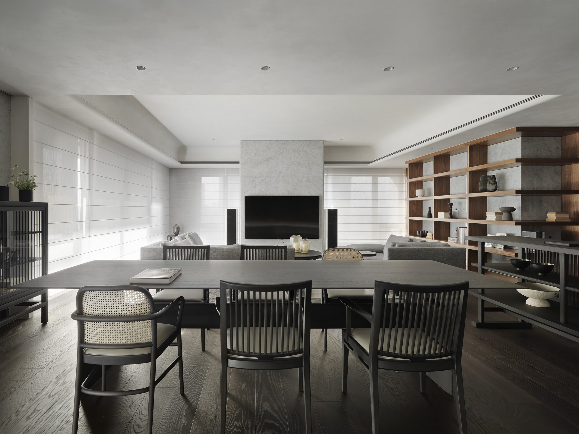 珥本設計｜忠泰老佛爺由餐廳望向客廳：全景皆為TIME & STYLE家具——深色長餐桌與藤編背黑框餐椅為前景，遠處TIME & STYLE灰色沙發群與大理石電視牆落於中軸，右側胡桃木層板書架牆延伸空間深度，深色橡木地板貫穿公領域，白色穿棒紗透光為主軸節奏