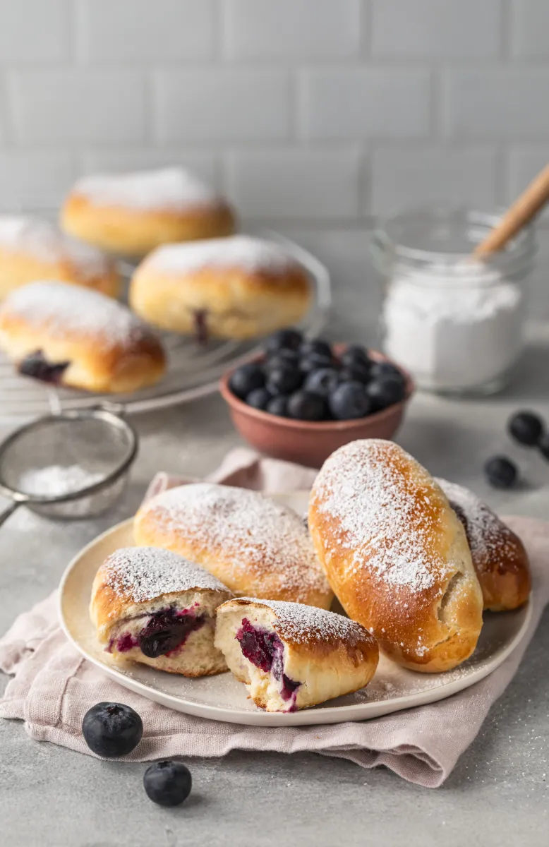 Jar of creamy almond butter surrounded by cinnamon stick, white chocolate shavings, raw sugar in a small dish, and a white creamer on a marble surface.
