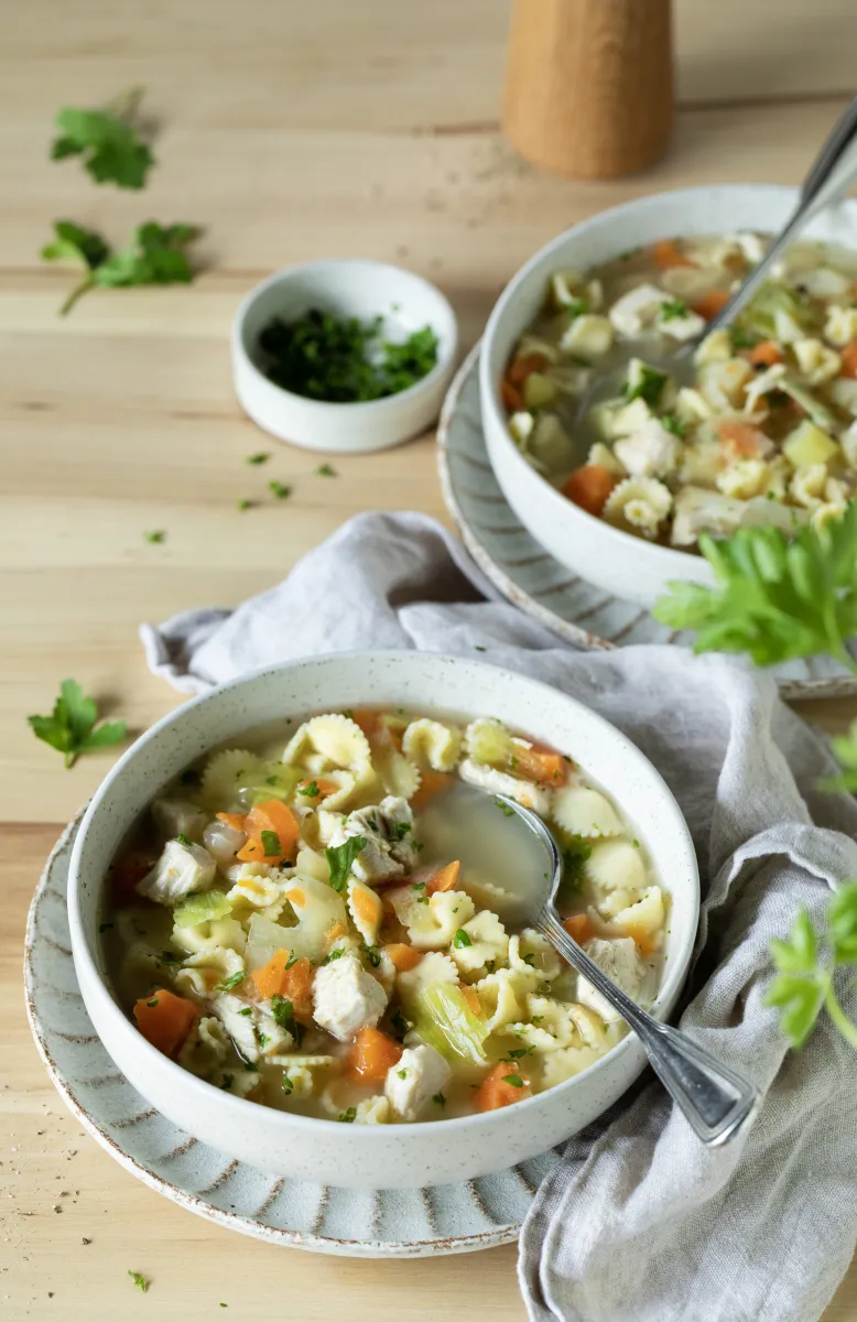 Hand pouring creamy red sauce from a metal container into a bowl of cooked penne pasta on a marble countertop.
