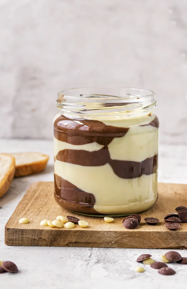 Five cinnamon sugar-coated baked apple fritters on parchment in a black tray next to one on a white plate and crumbs on a gray surface.
