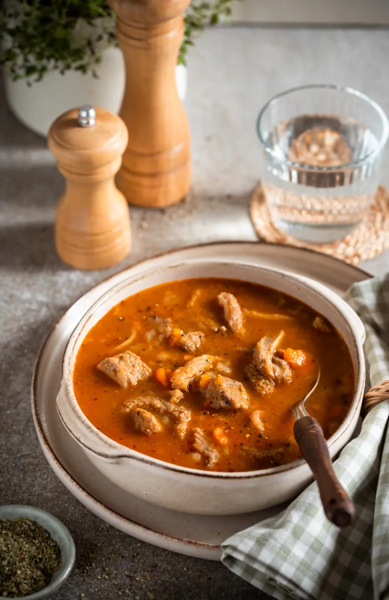 Cooked chicken breasts with cherry tomatoes and basil leaves in a black cooking tray on a tiled surface with herbs and tomato sauce beside it.