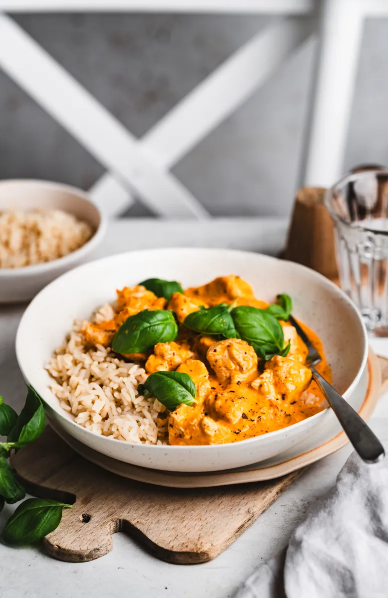 Bowl of tomato-based tortellini soup garnished with fresh basil leaves and black pepper, with a spoon inside the bowl.