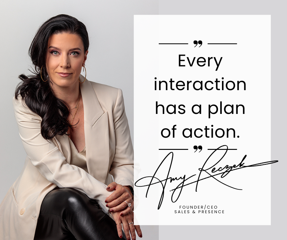 A tiny knitted gnome with a red hat and blue sleeves sits on a grey surface, knitting with miniature needles while pulling yarn from a pink ball of wool.