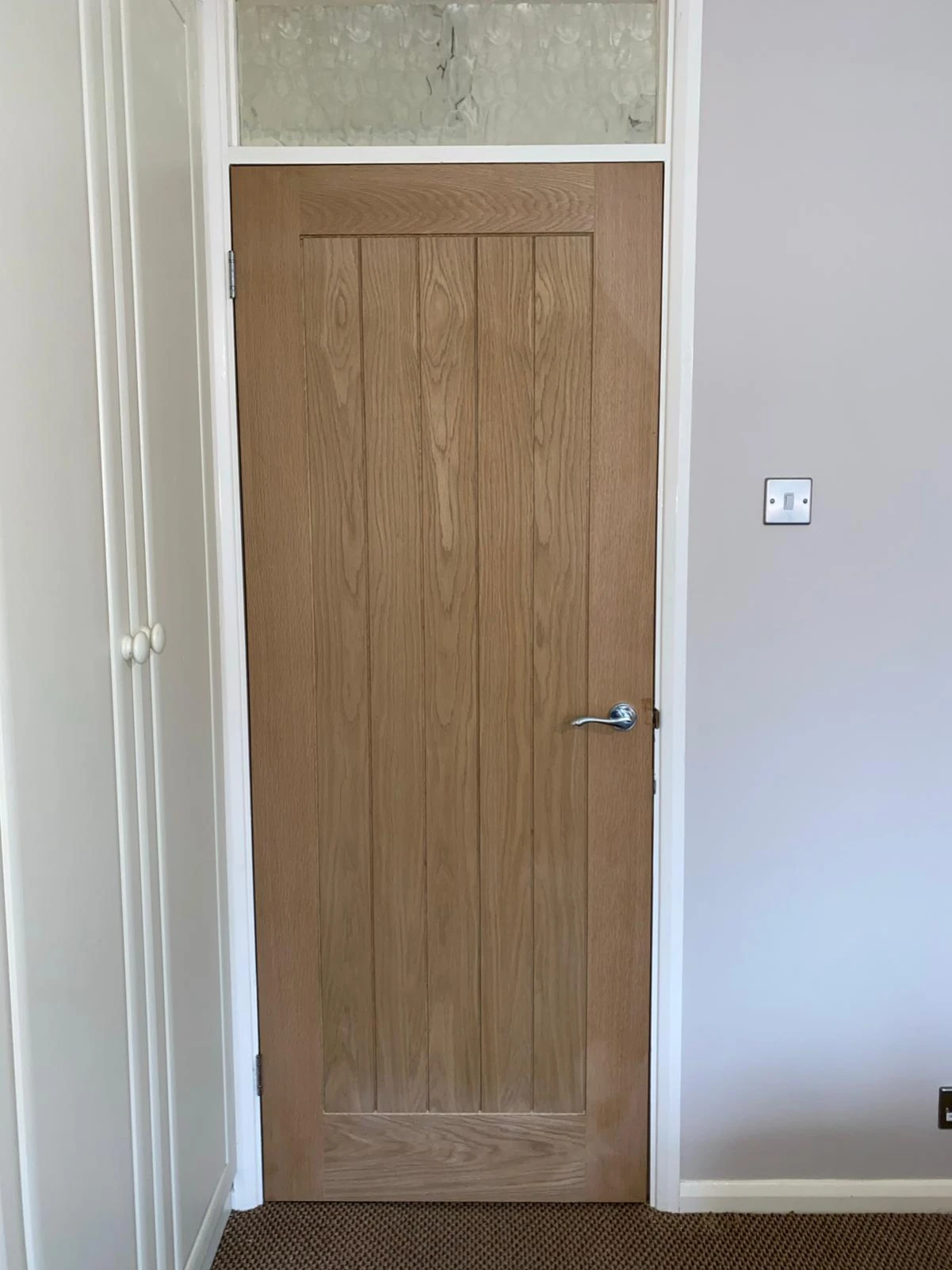 Closed wooden interior door with vertical panels and silver handle in a beige-walled room.