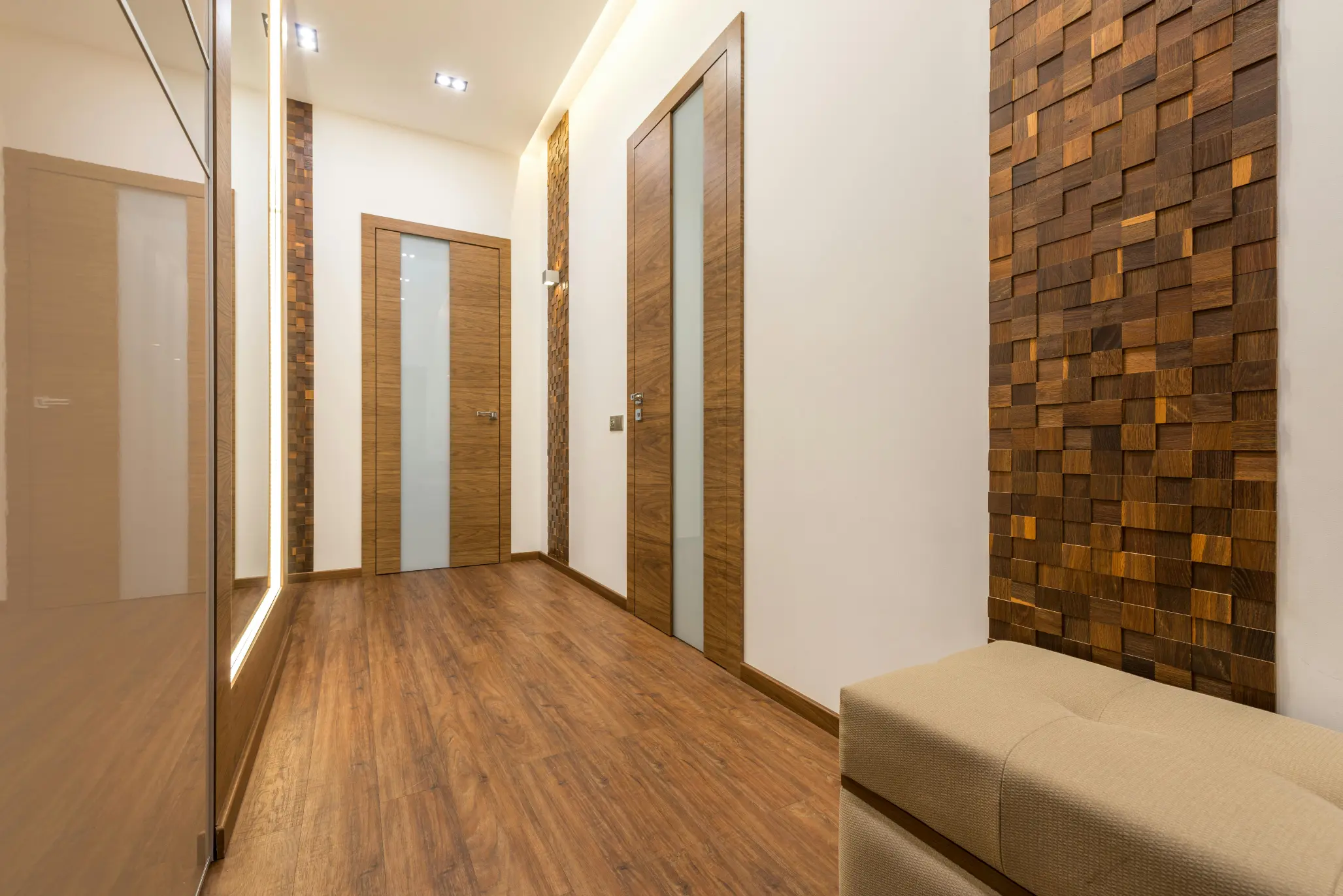 Modern hallway with wooden floor, two wooden doors with frosted glass panels, textured wooden wall accents, and a beige upholstered bench.