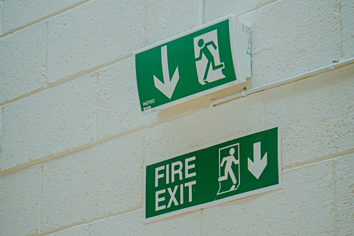 Two green fire exit signs on a beige brick wall pointing downwards.