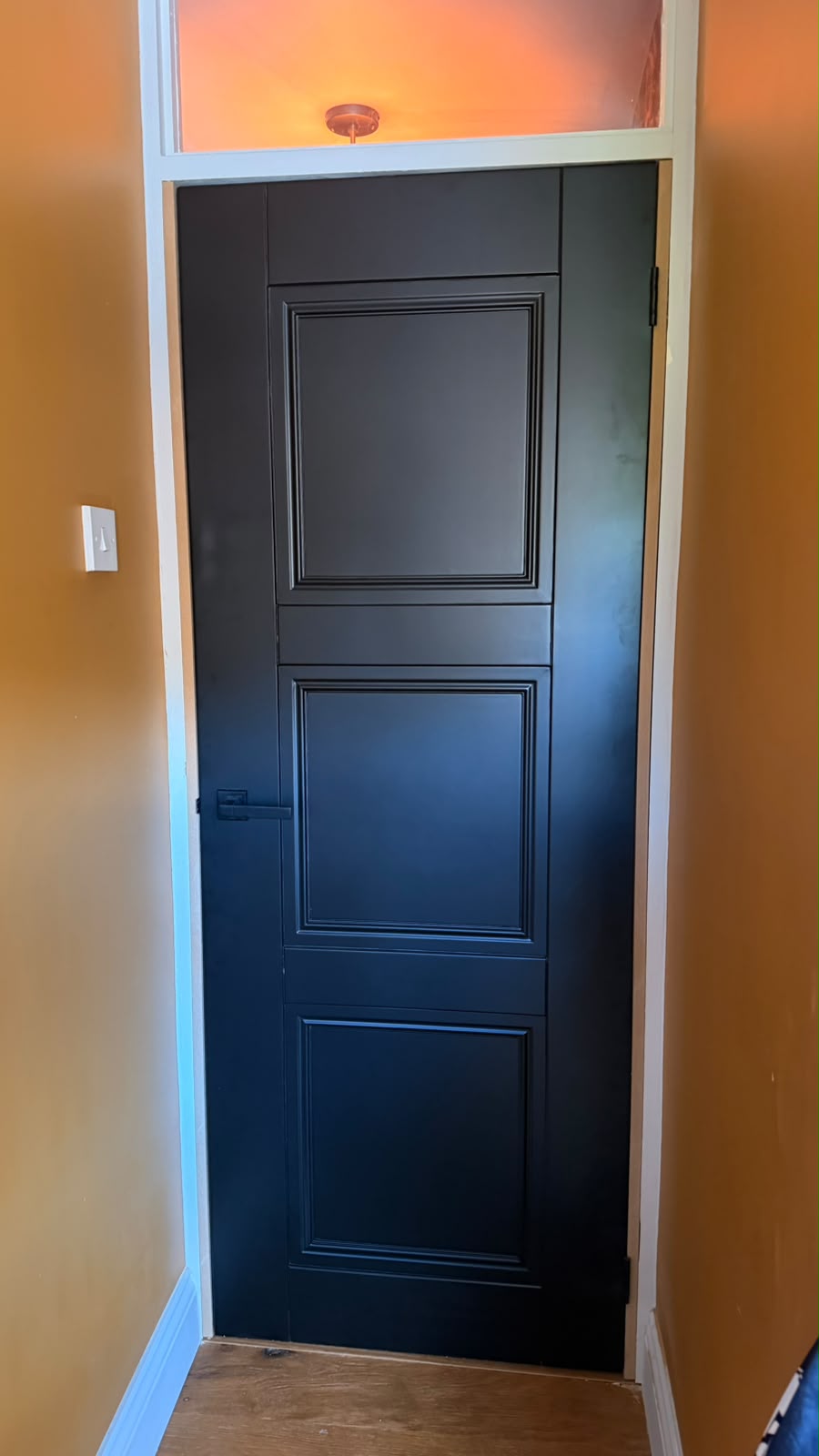 Black Elegance Ripley internal door with a black lever handle in a white frame beside ochre walls in Haslemere