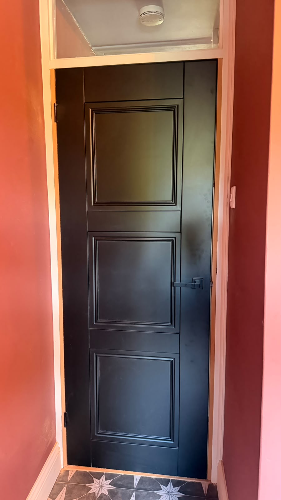 Black Elegance Ripley internal door with a black lever handle beneath a glazed fanlight beside coral walls in Haslemere