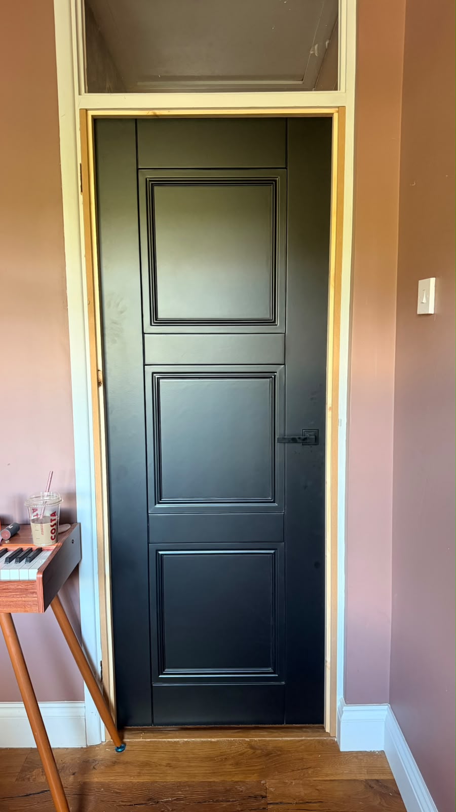 Black Elegance Ripley internal door with three moulded panels and a black lever handle beside pink walls in Haslemere